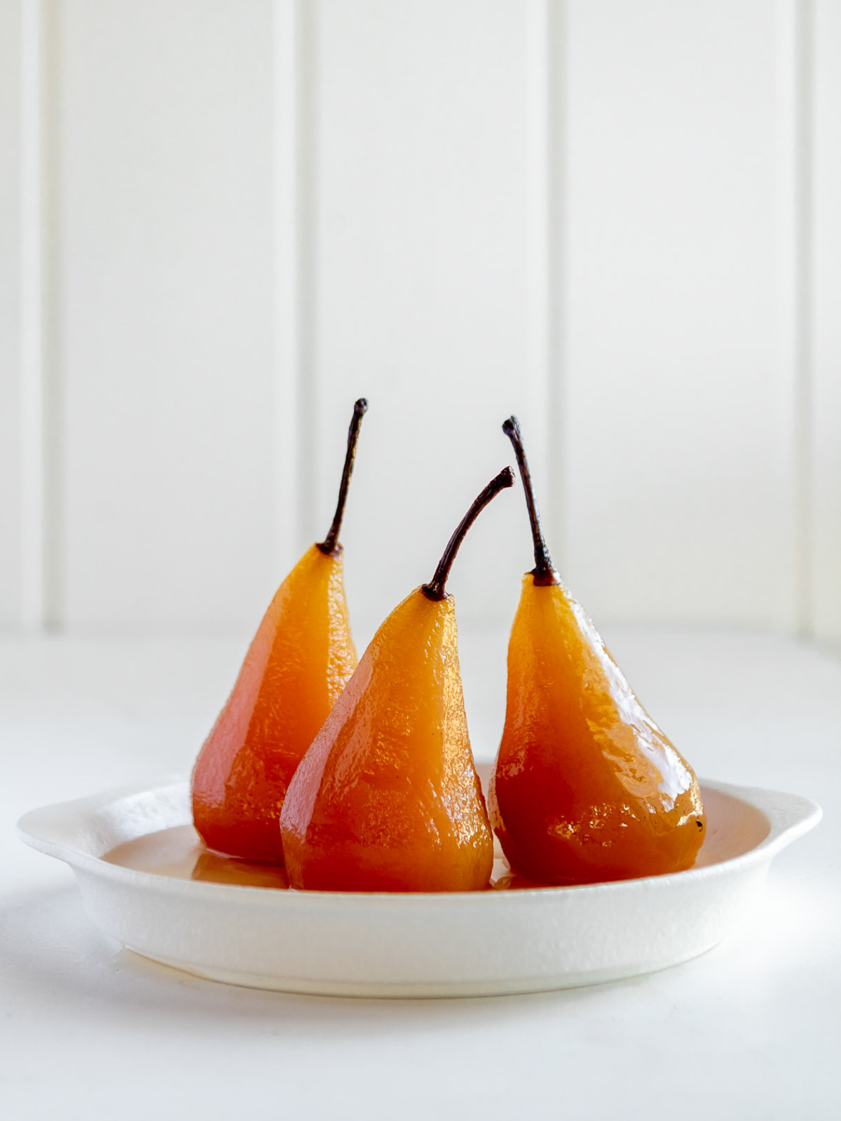Poached pears in a white plate, in a sugar syrup poaching liquid.