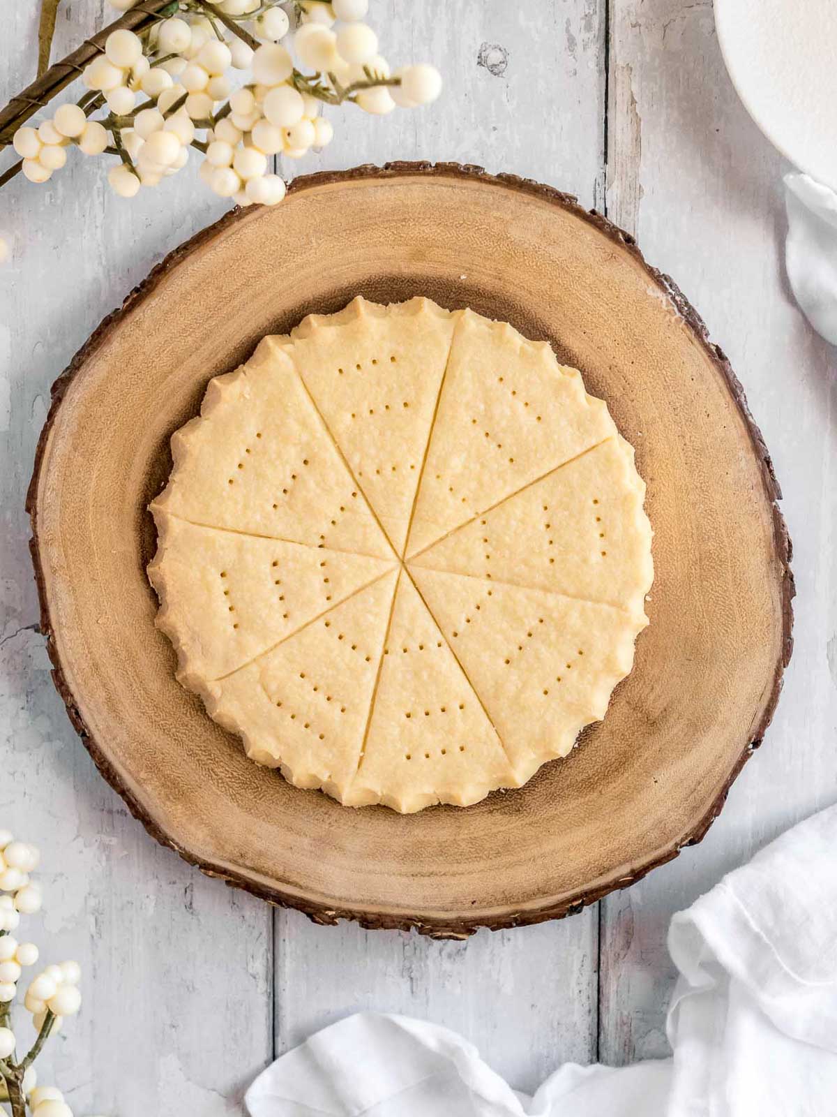 A round disc of traditional Christmas shortbread on a rustic wooden cake stand, golden and sugar-dusted, ready to slice and share