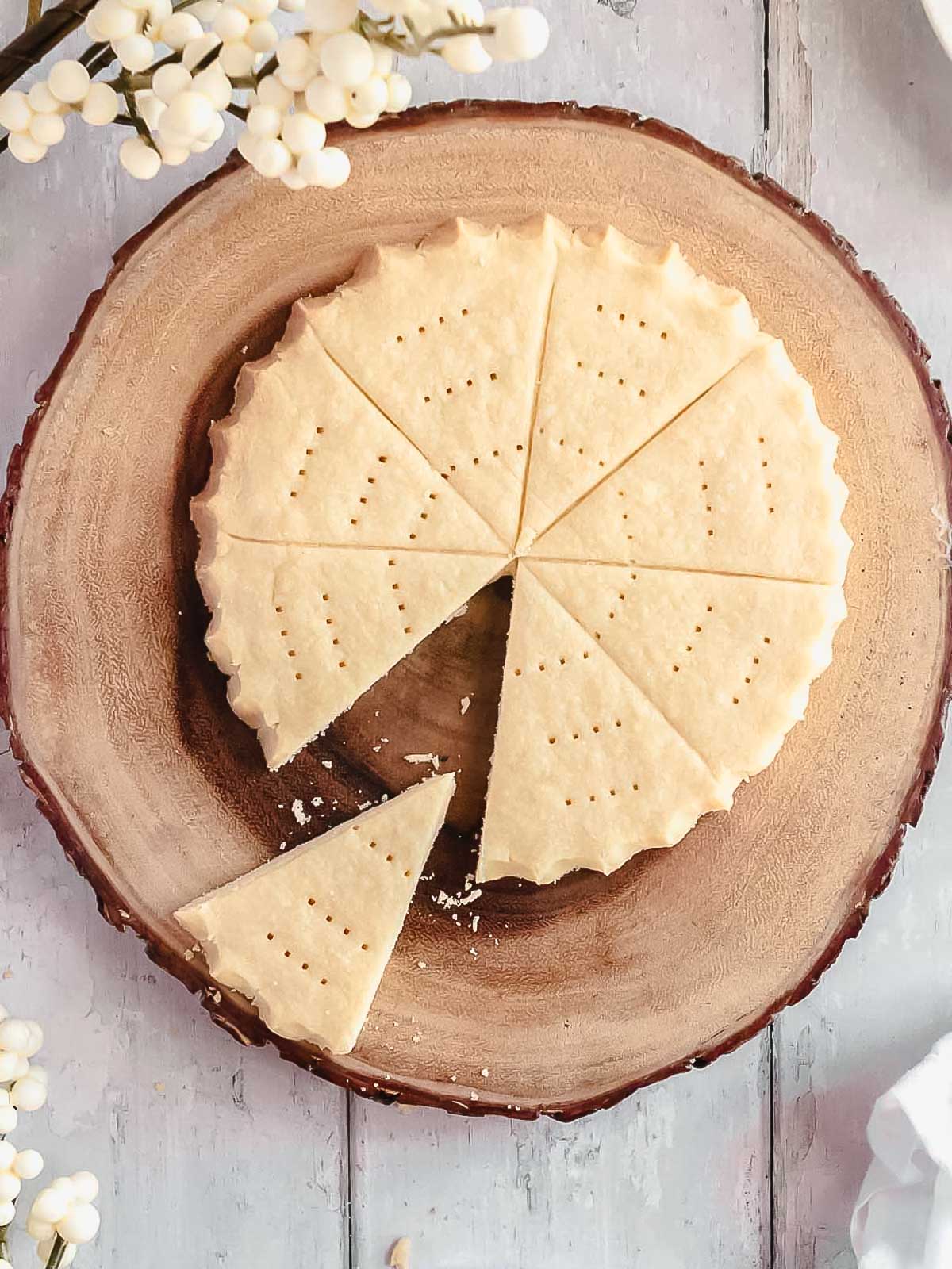 A round disc of traditional Christmas shortbread on a rustic wooden cake stand, golden and sugar-dusted, ready to slice and share