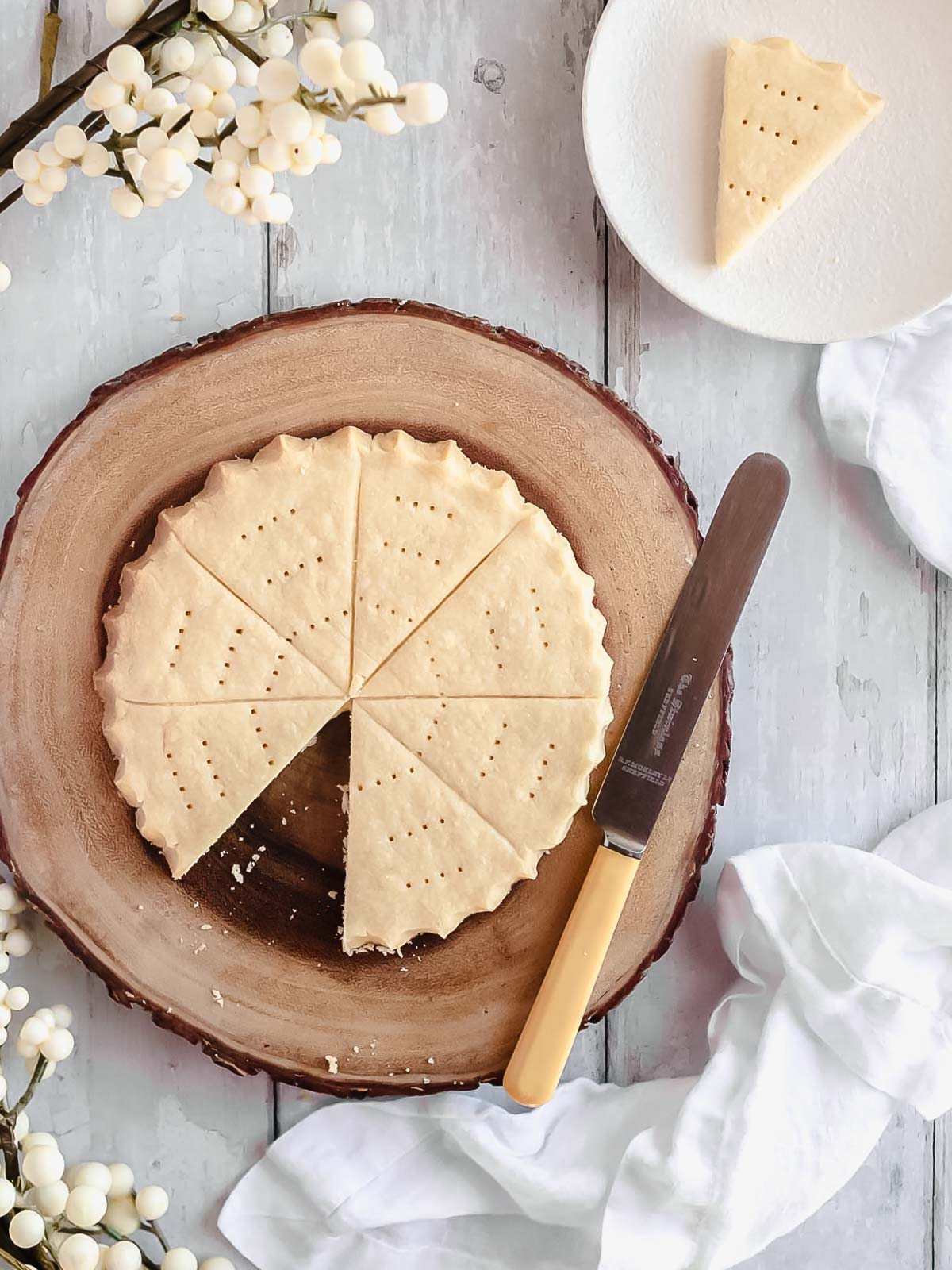 A round disc of traditional Christmas shortbread on a rustic wooden cake stand, golden and sugar-dusted, ready to slice and share