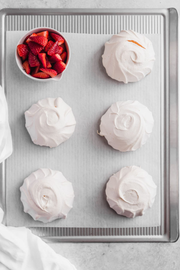 individual pavlovas on baking tray with strawberries
