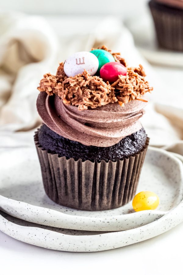 single chocolate cupcake with swirls chocolate frosting topped with coconut nest and easter eggs