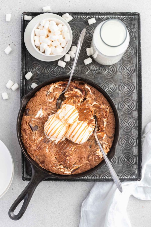 skillet cookie on a tray with marshmallow and a bollte of milk