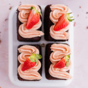 Four mini chocolate cakes decorated with strawberry buttercream and fresh strawberries.