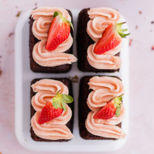 Four mini chocolate cakes decorated with strawberry buttercream and fresh strawberries.