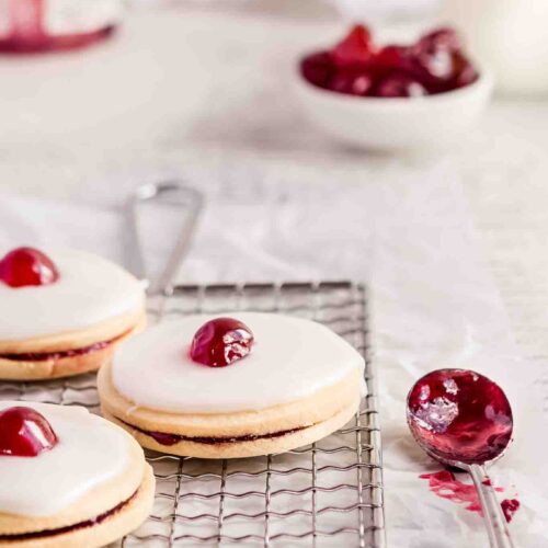 3 sandwich cookies topped with white icing and a glace cherry