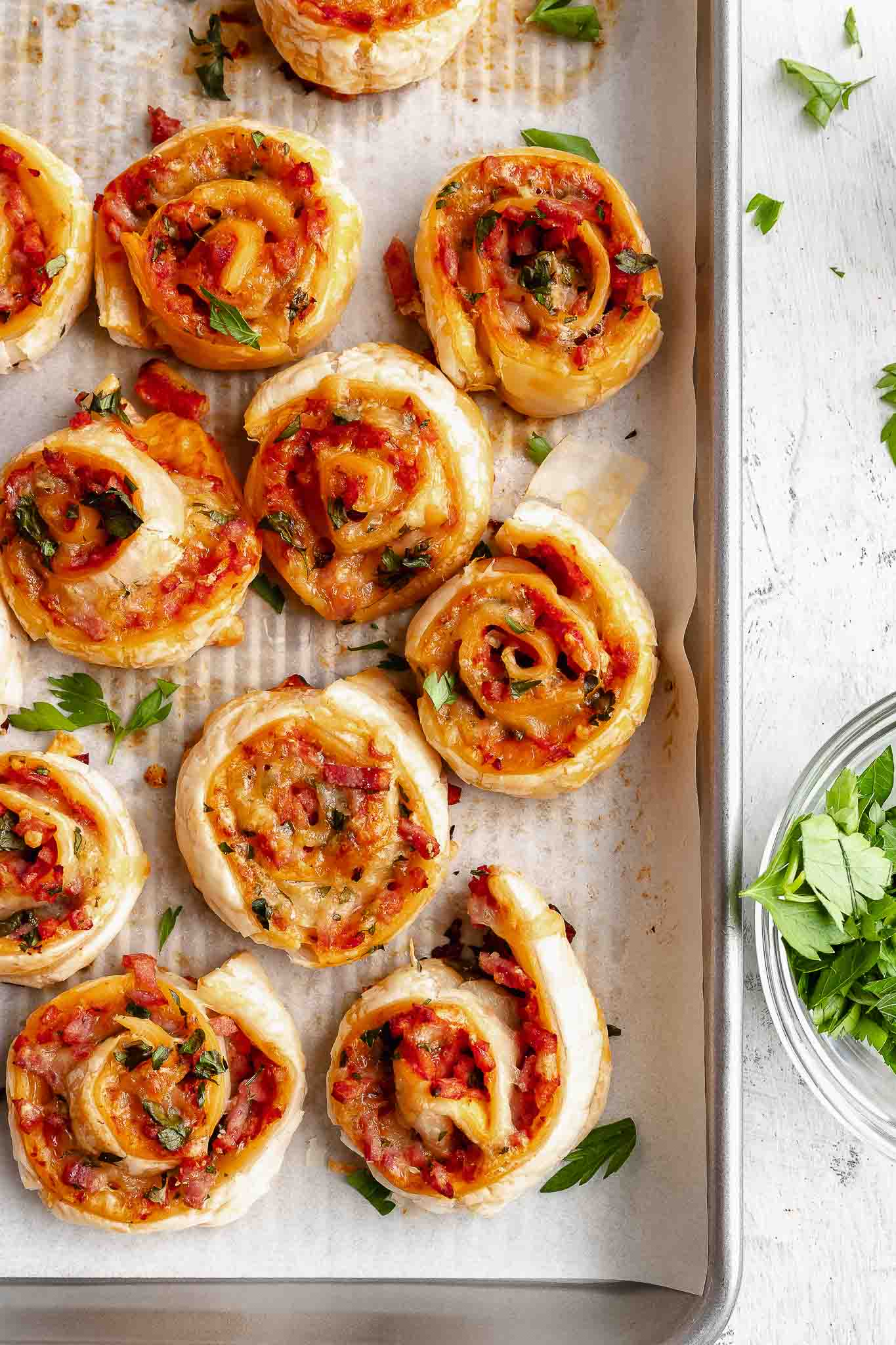 overhead shot of pizza pinwheels on a tray, with parsley in a bowl on the side