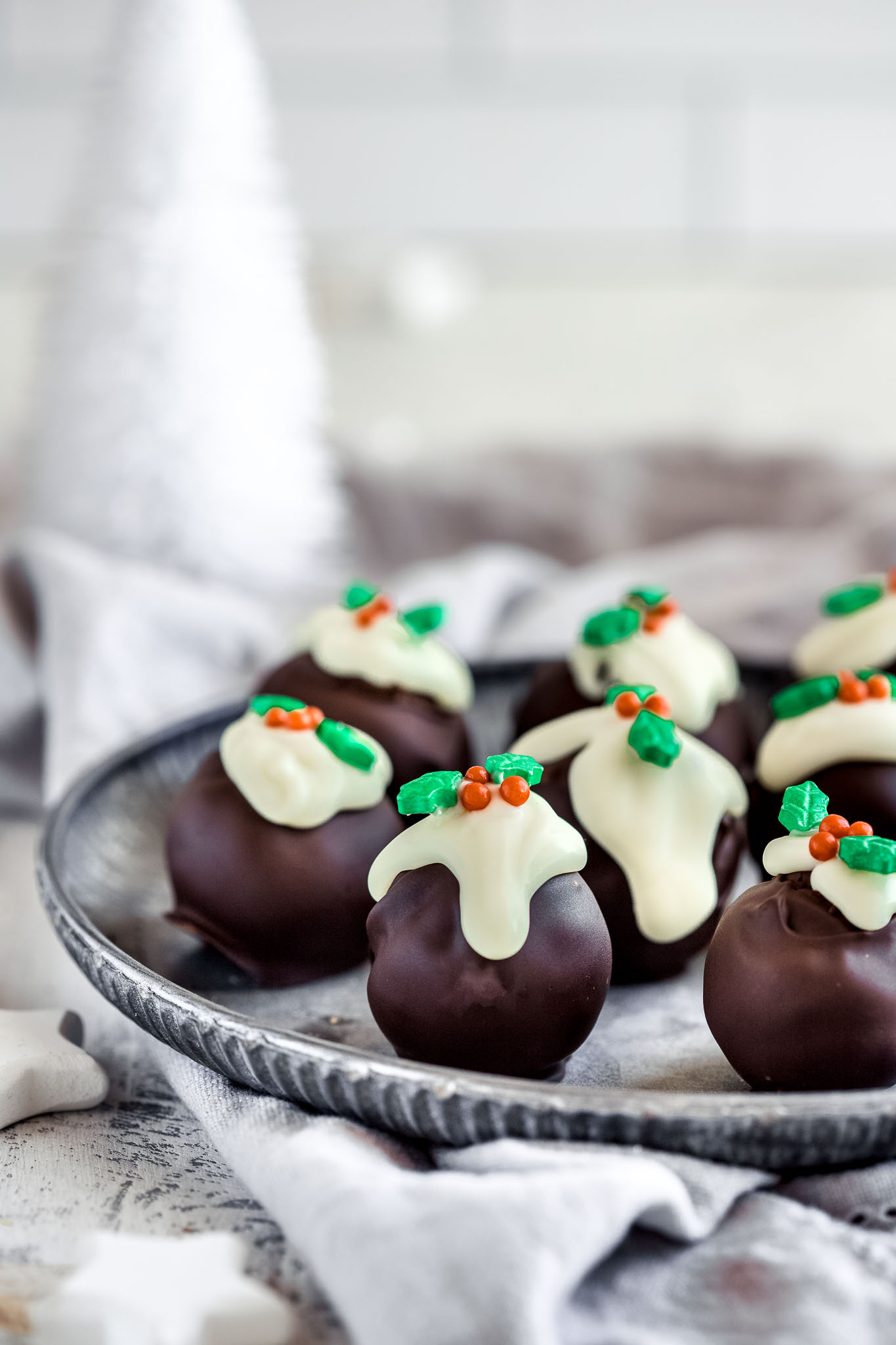 mini Christmas pudding truffles on a round vintage tray and a white Christmas tree in the background