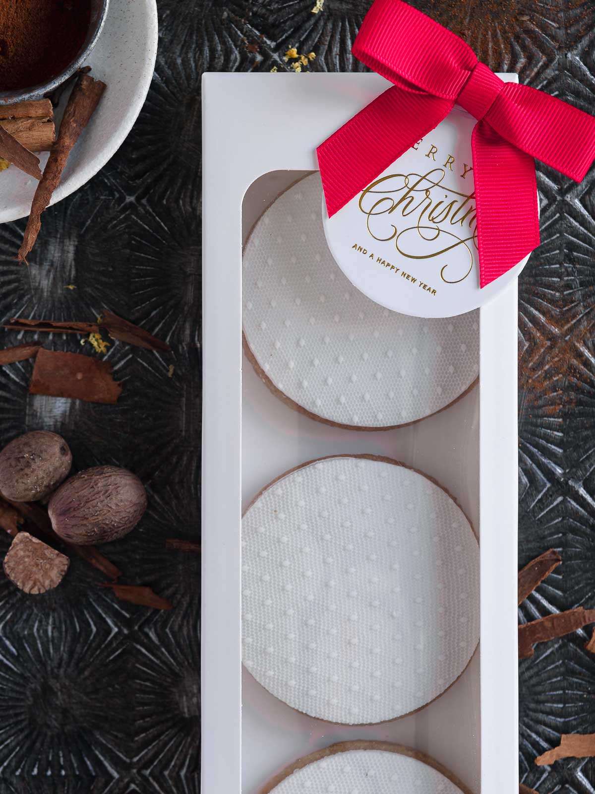 a white cookie box with 3 decorated speculaas sugar cookies, finished with a red bow and a Christmas gift tag