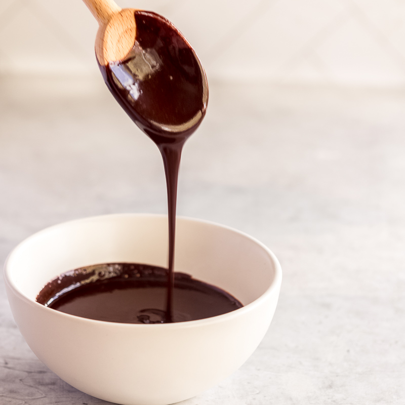 chocolate glaze dripping off a spoon into a white bowl