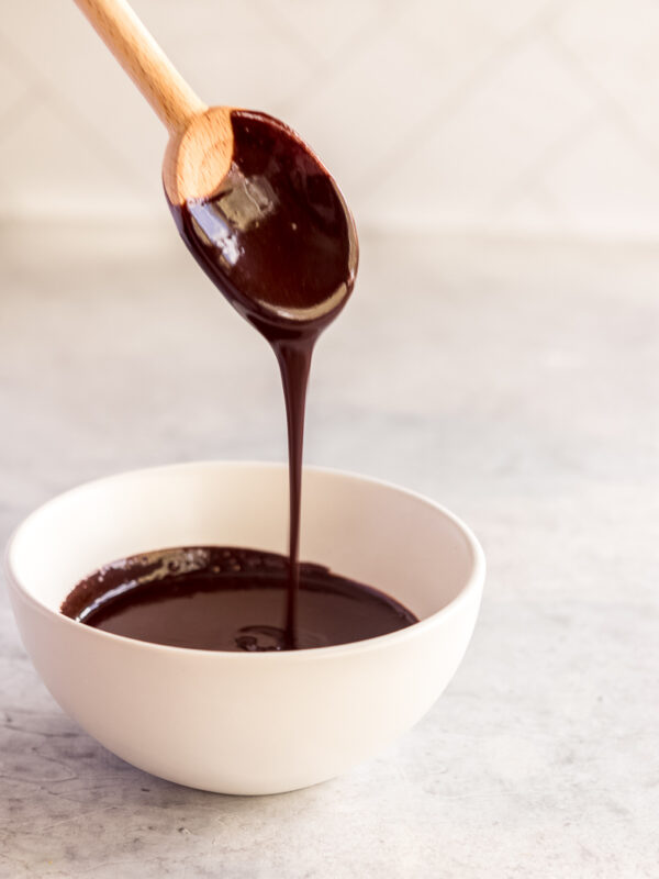 chocolate glaze dripping off a wooden spoon into a white bowl