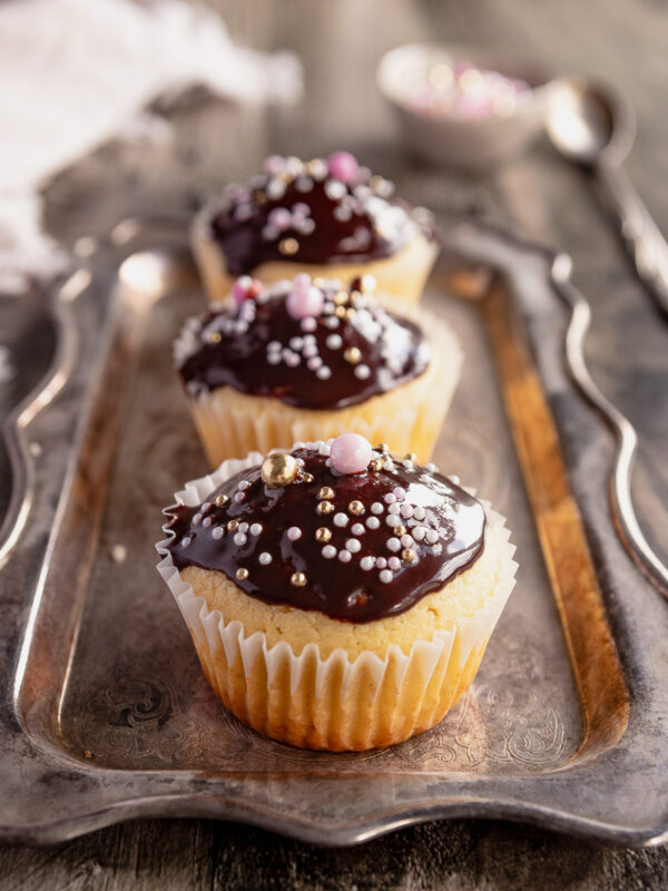 3 vanilla cupcakes topped with chocolate glaze and sprinkles