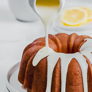 a small white jug being used to pour vanilla glaze over a bundt cake