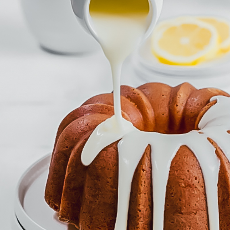 a small white jug being used to pour vanilla glaze over a bundt cake