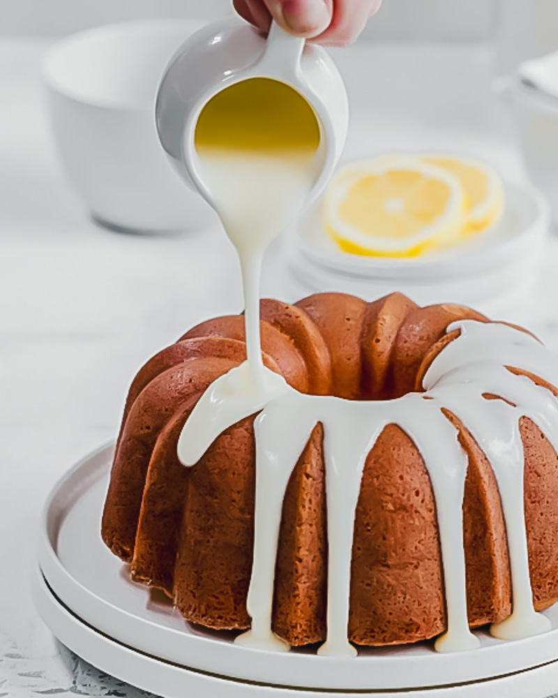 vanilla bean glaze being poured from a small white jug, over a lemon bundt cake