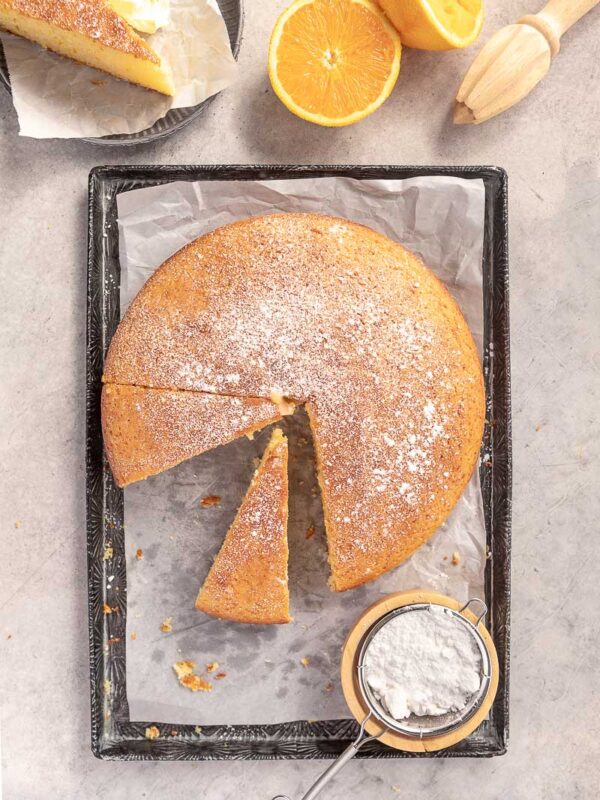 overhead shot of an orange cake, dusted with icing sugar and cut into wedges