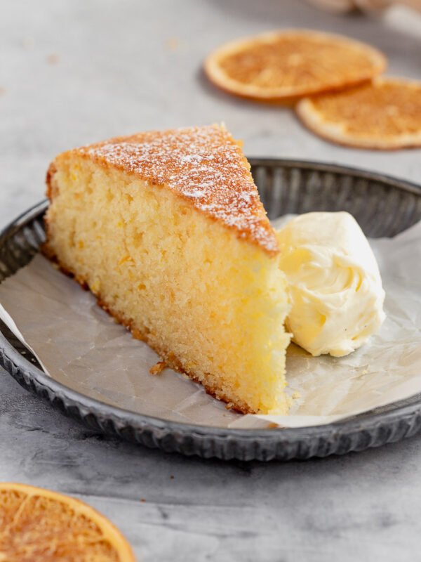 a slice of orange cake on a small plate, served with cream