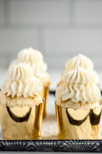How to make the softest vanilla cupcakes, with four cupcakes in gold papers, topped with vanilla buttercream.