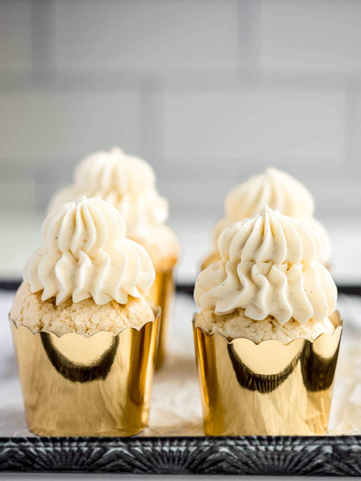 How to make the softest vanilla cupcakes, with four cupcakes in gold papers, topped with vanilla buttercream.