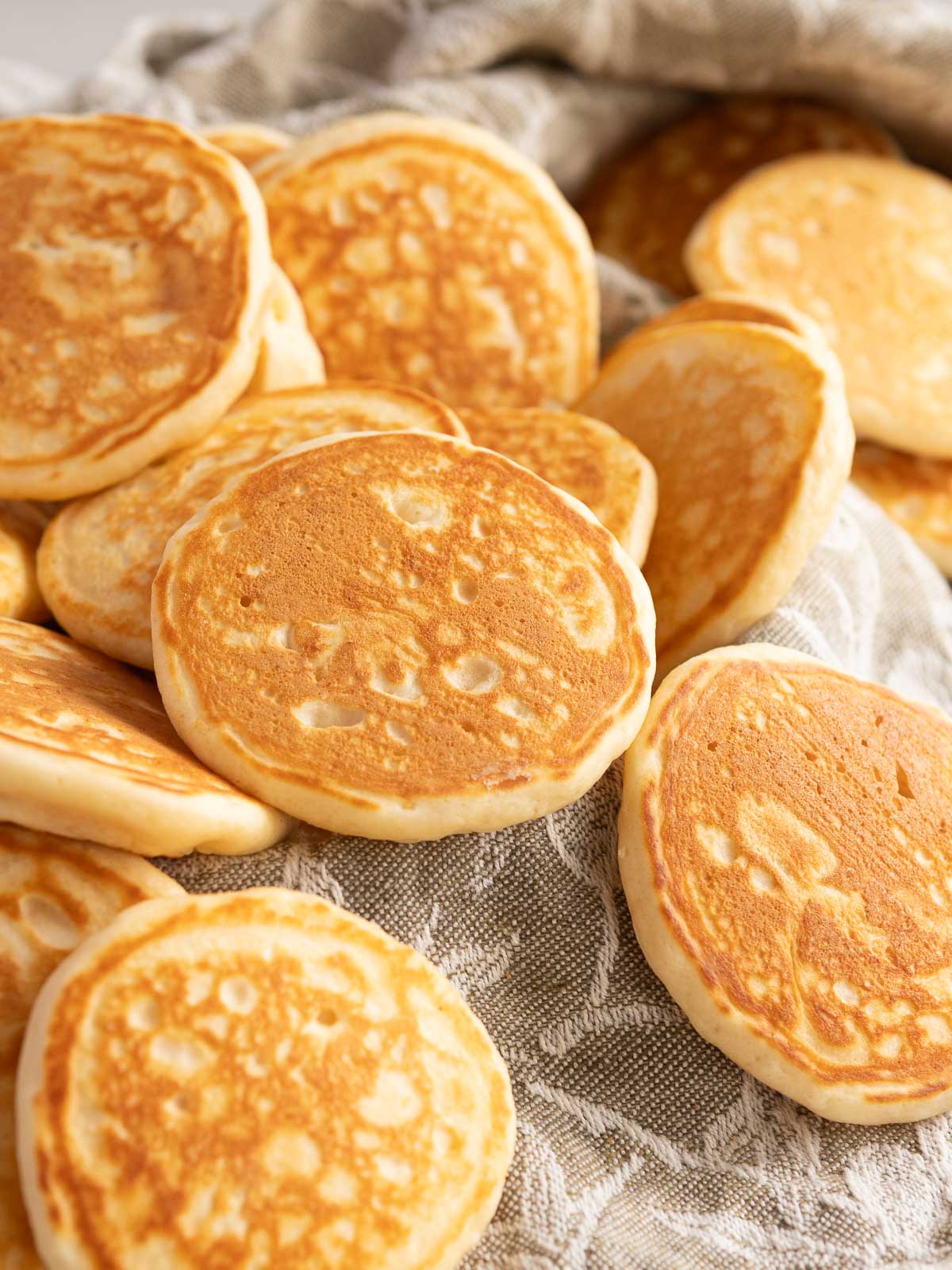 Cooked pikelets resting on a linen tea towel.