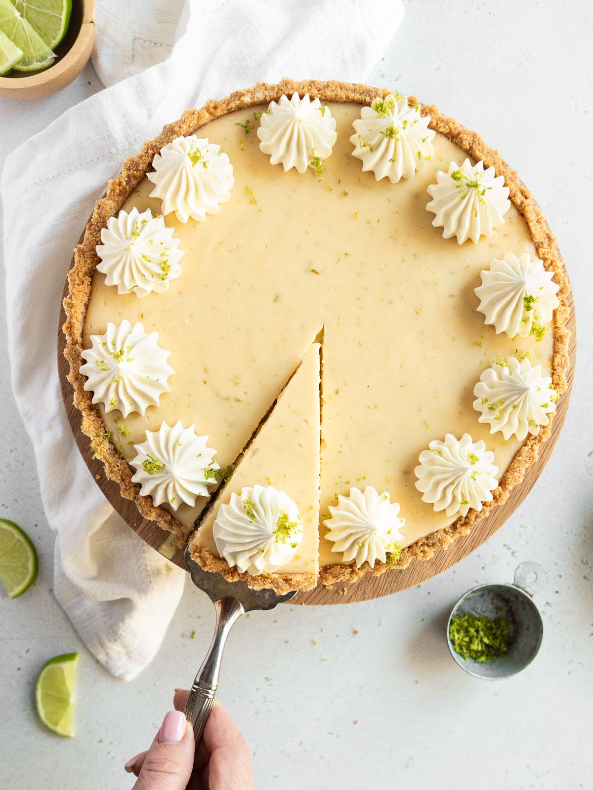 A whole gluten-free Key Lime Pie with a wedge being served, topped with whipped cream and garnished with lime zest.