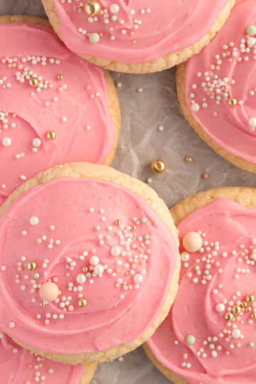 A tray of soft, pink frosted sugar cookies topped with colourful sprinkles – bakery-style cookies with thick, pillowy centres