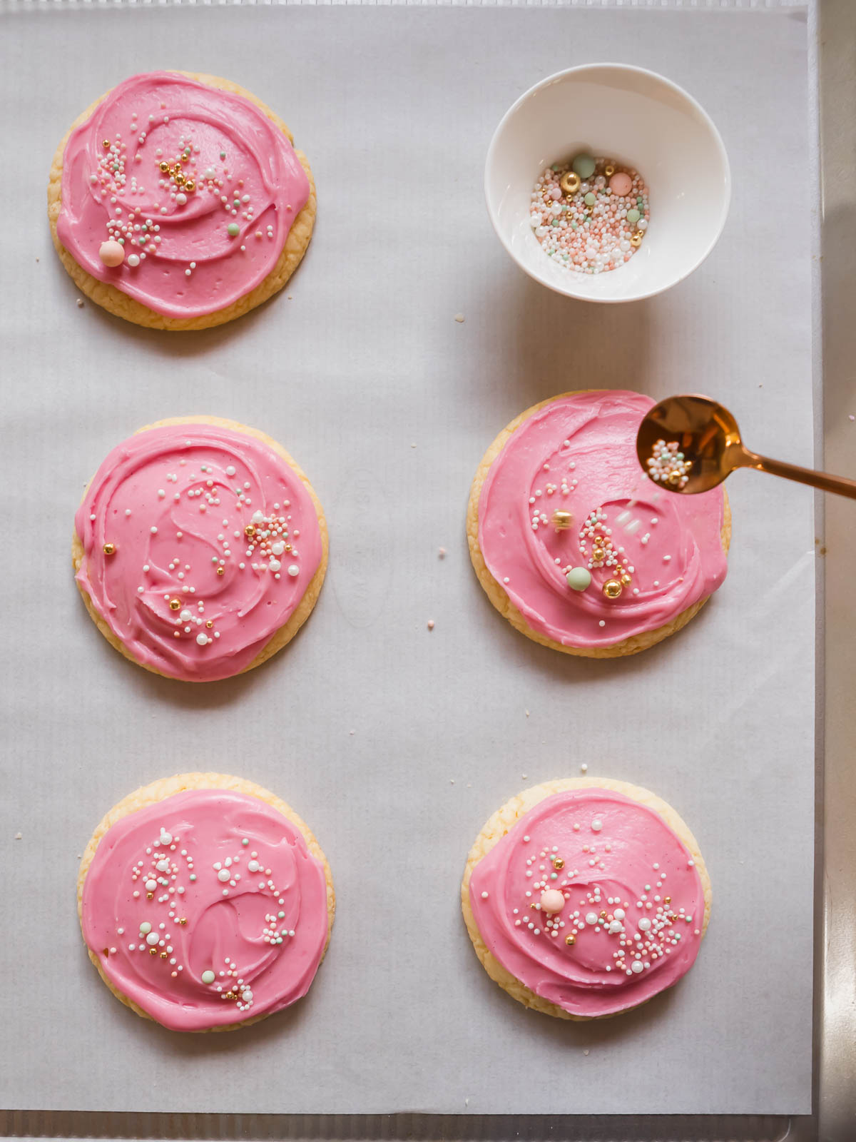 Soft sugar cookies topped with pastel pink frosting and colourful sprinkles.