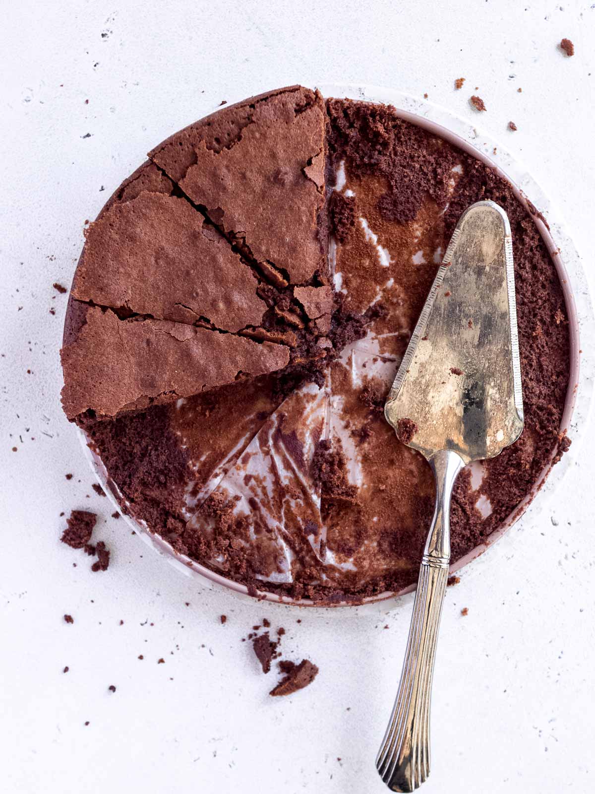 A large chocolate fudge cake that has been cut into 12 slices to be served as a dessert. Three slices remain on the plate.