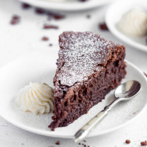 A slice of fudgy chocolate cake, served with chantilly cream and a dusting of icing sugar.