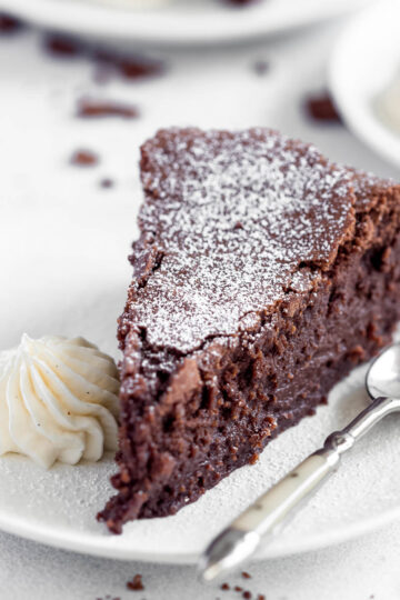 A slice of fudgy chocolate cake, served with chantilly cream and a dusting of icing sugar.