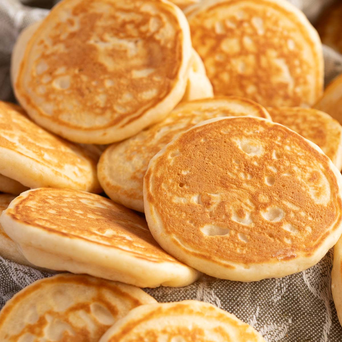 Mini pancakes or pikelets, resting on a linen tea towel to serve.