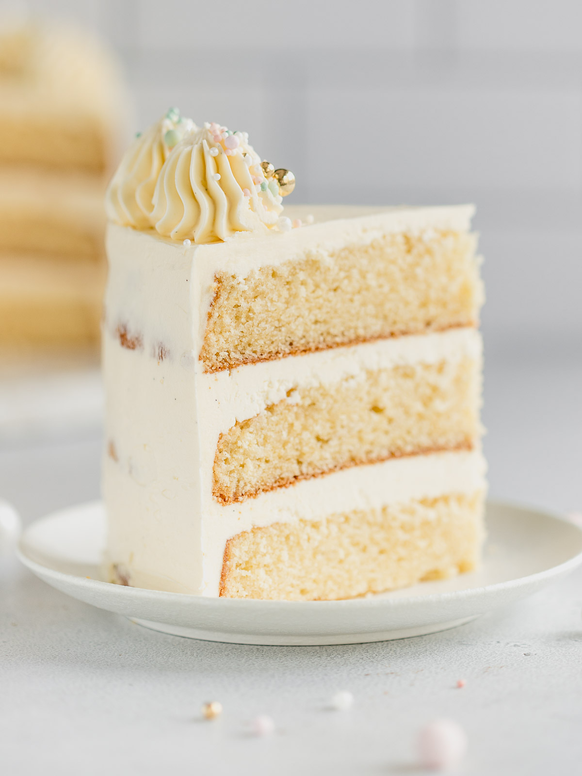 A slice of decorated 3 layer vanilla cake on a small white plate.