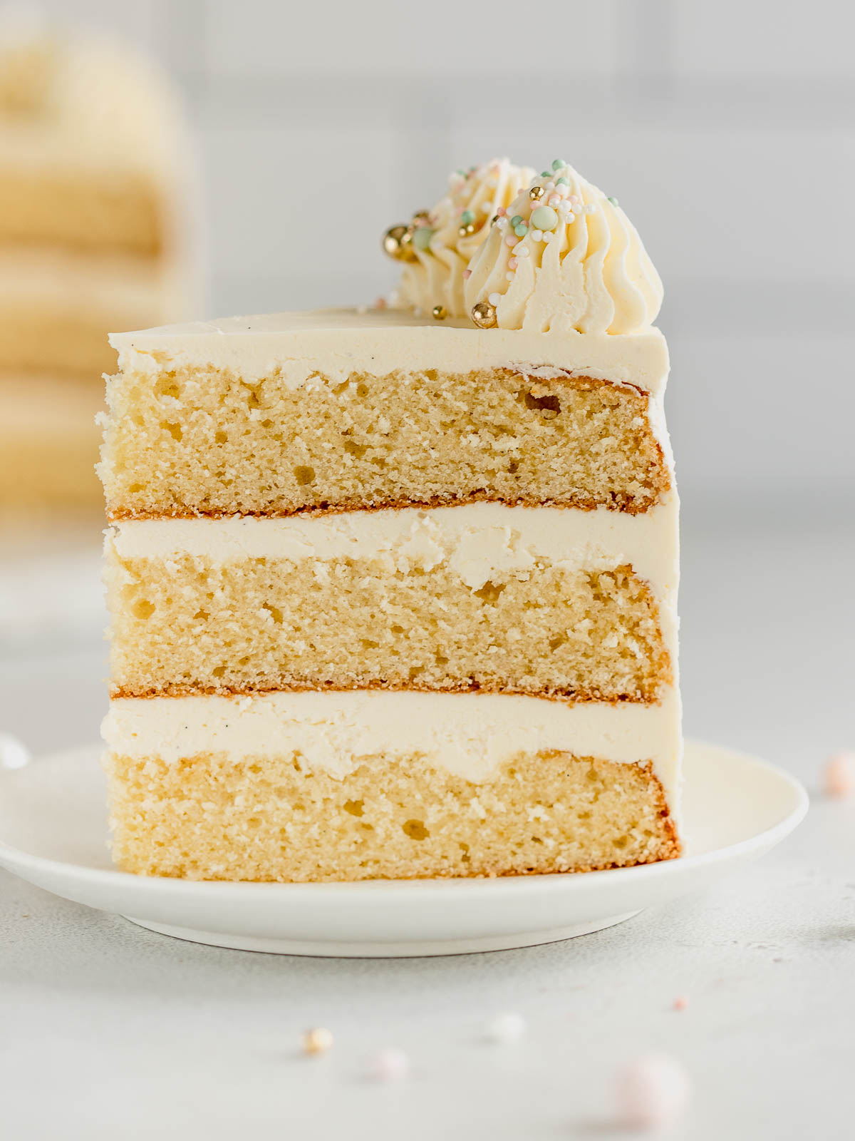 A slice of decorated 3 layer vanilla cake on a small white plate.