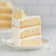 A slice of decorated 3 layer vanilla cake on a small white plate.