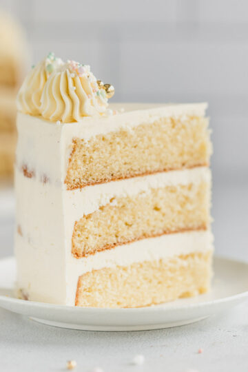 A slice of decorated 3 layer vanilla cake on a small white plate.