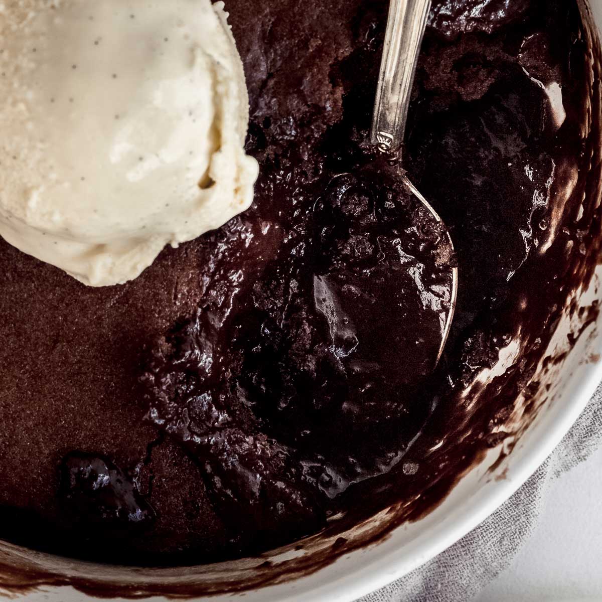 A close up shot of a chocolate self saucing pudding, topped with vanilla ice cream. 