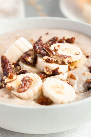 A bowl of creamy porridge, topped with candied nuts and banana.