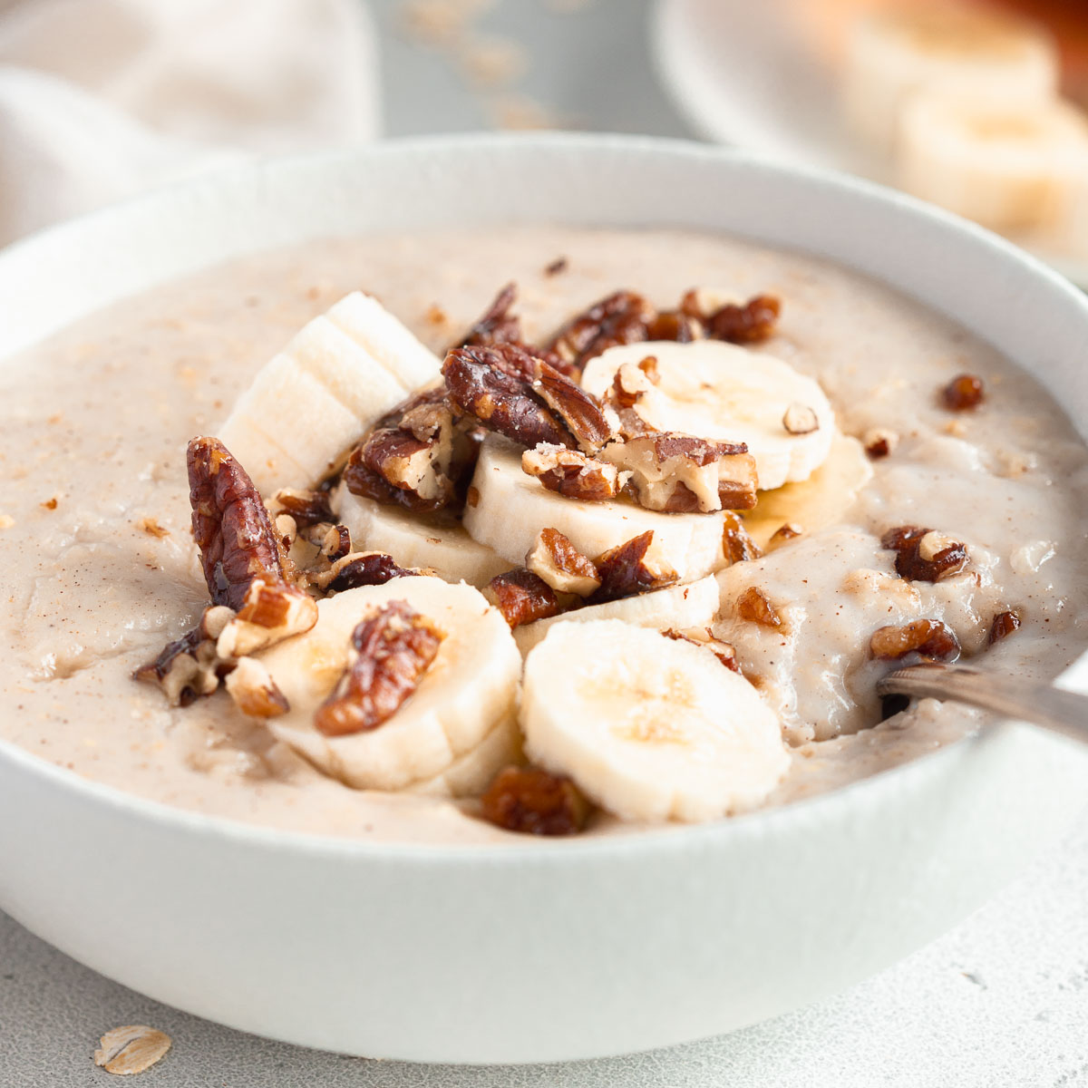 A bowl of creamy porridge, topped with candied nuts and banana.