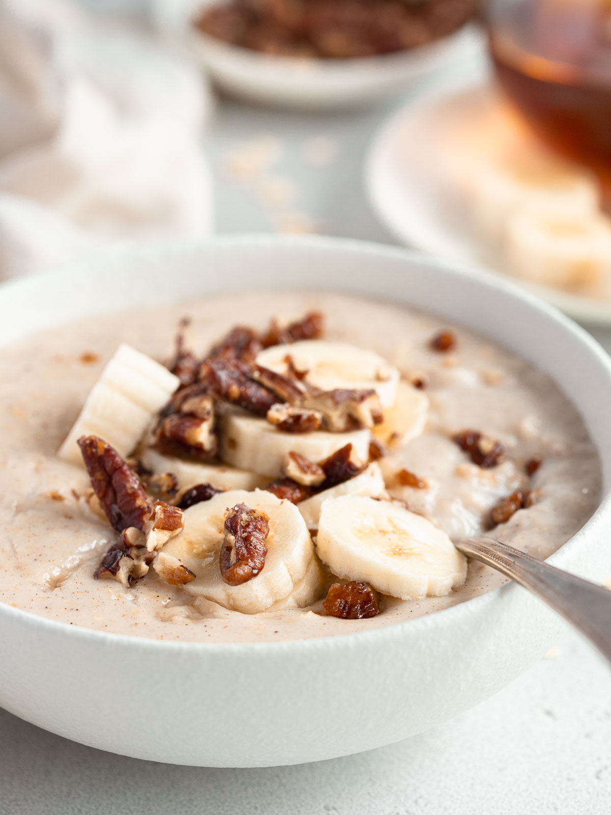 A bowl of creamy porridge, topped with candied nuts and banana.