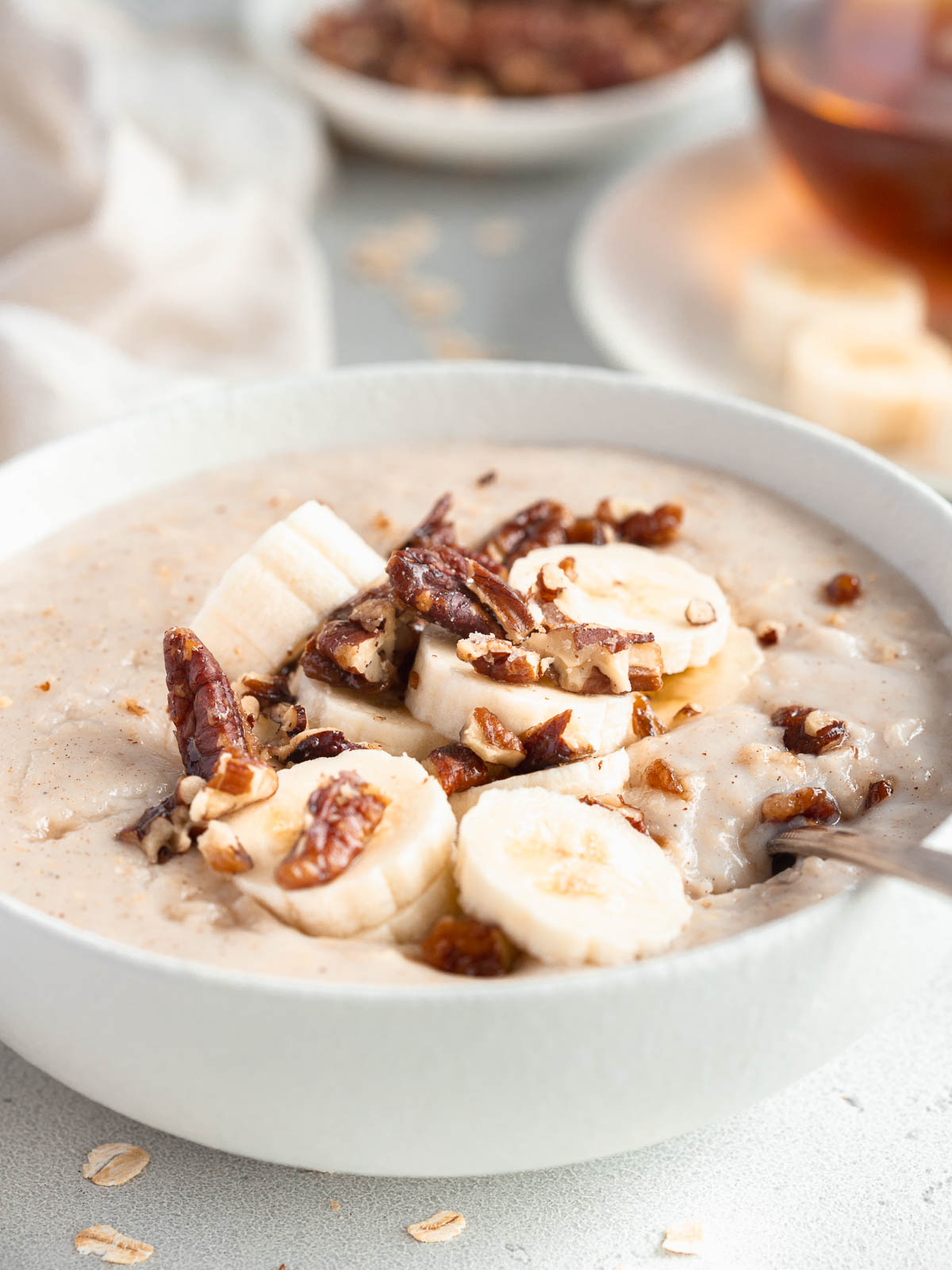 A bowl of creamy porridge, topped with candied nuts and banana.