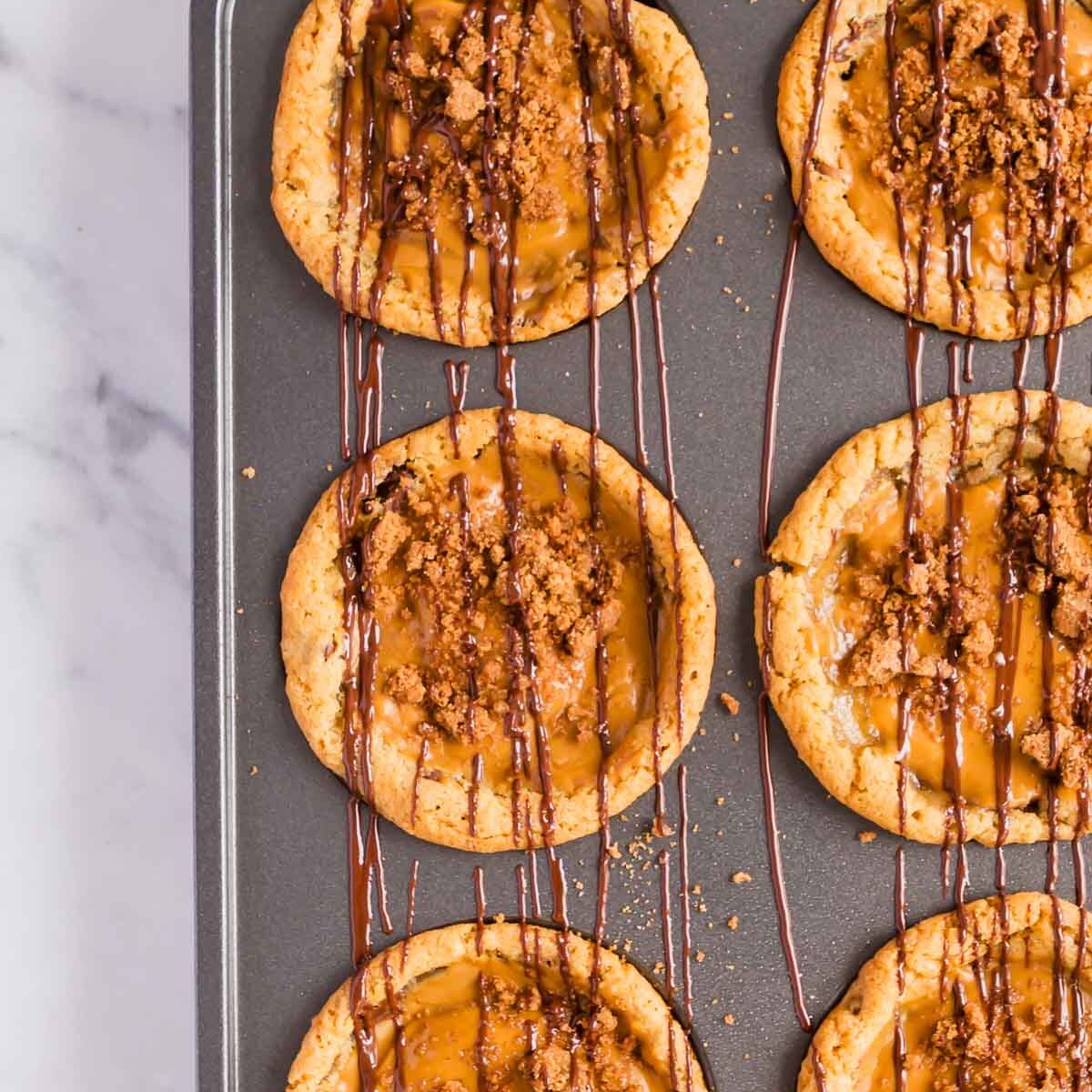 Sprinkle the biscoff stuffed cookies with crushed biscuits and drizzle with melted chocolate.