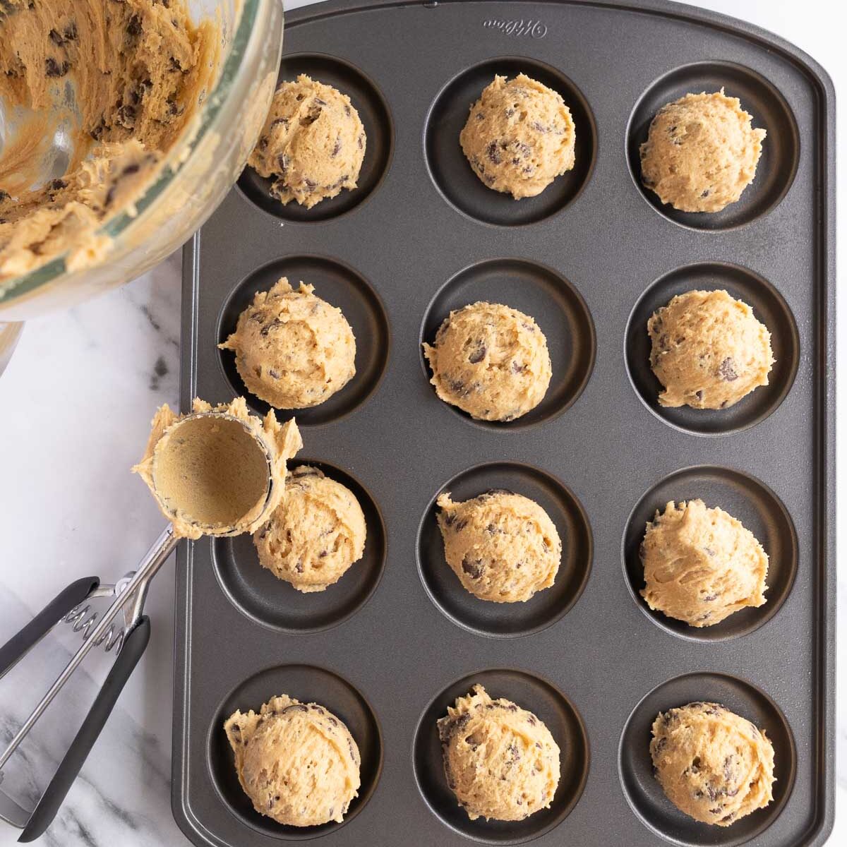 Scooping cookie dough into a muffin top pan.