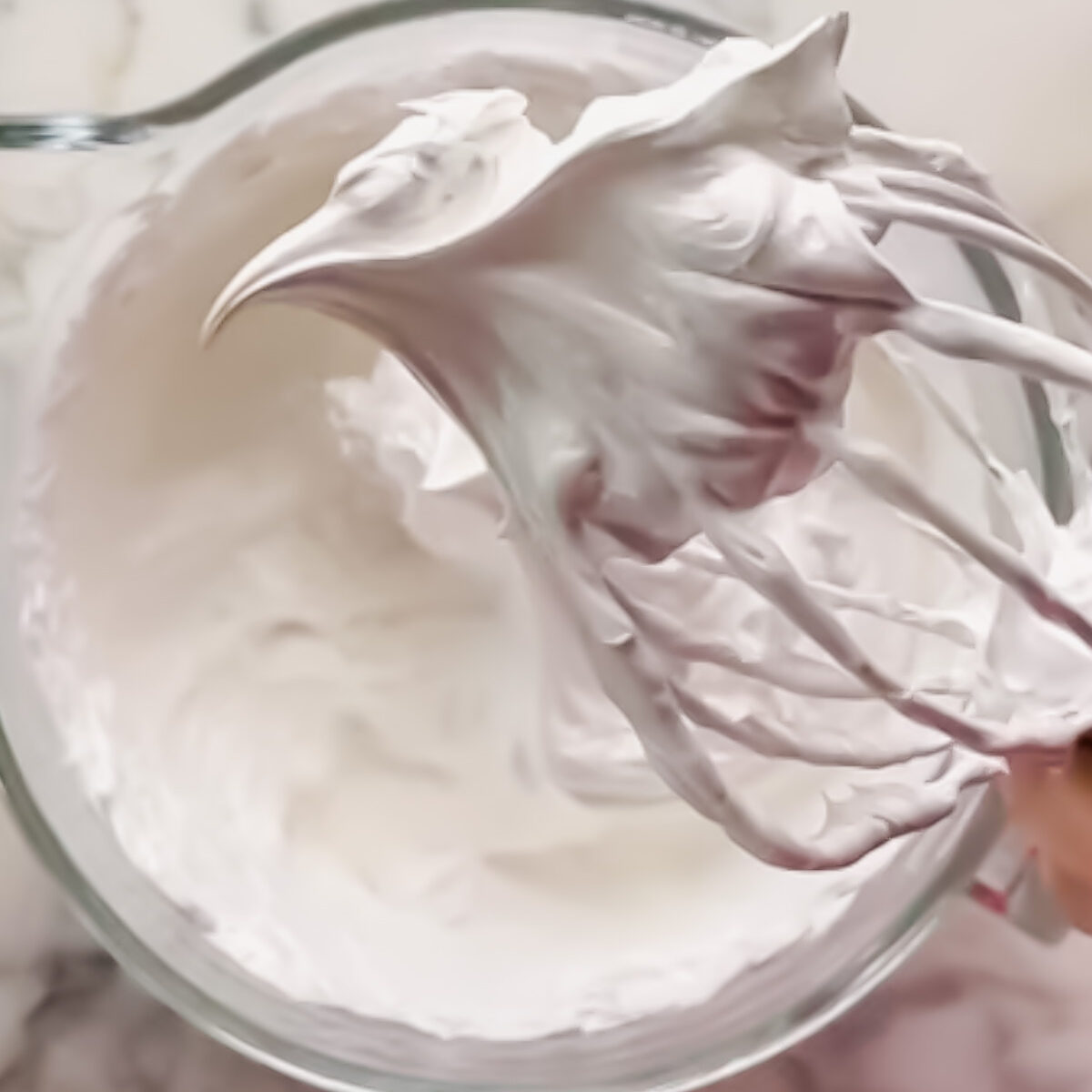 Beating pavlova meringue, then adding caster sugar gradually and whipping to a glossy, thick meringue.