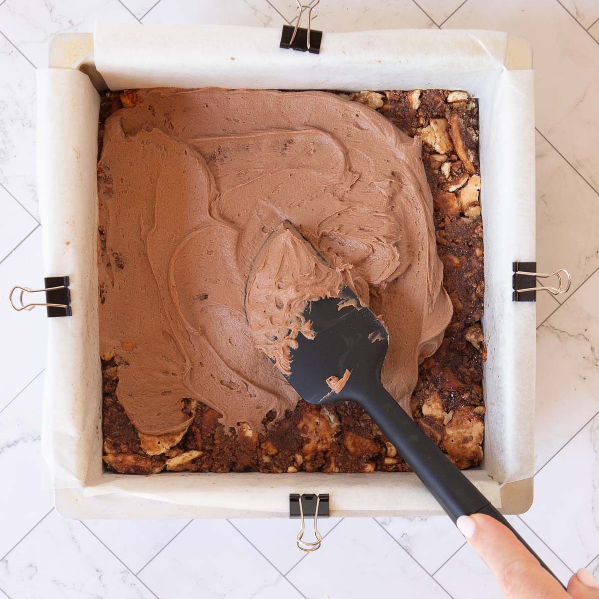 Spreading chocolate frosting over the hedgehog slice mixture.