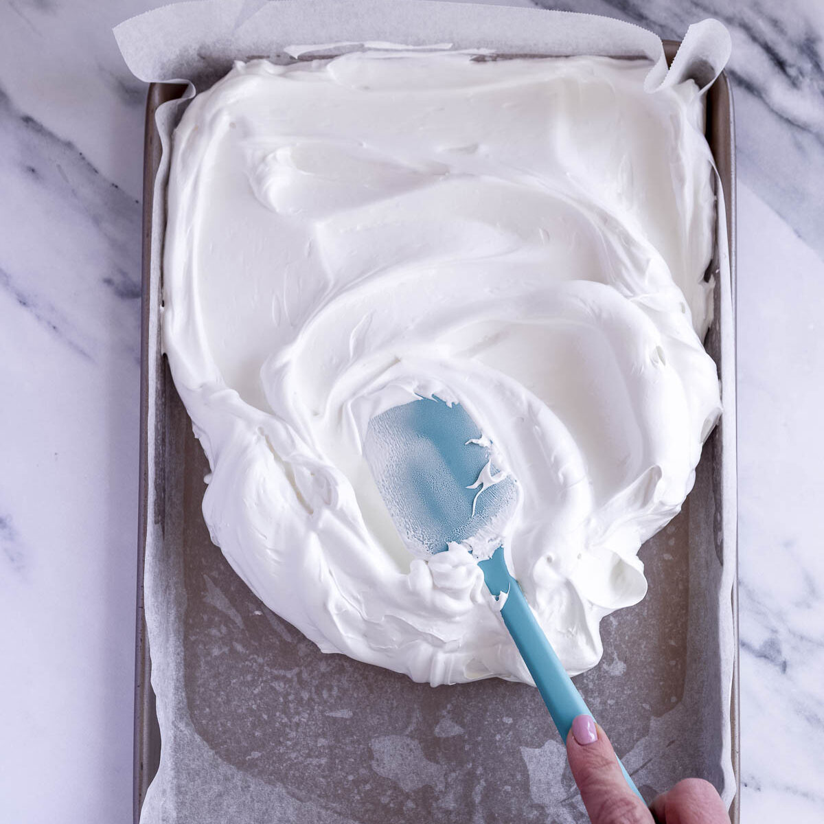 Spreading meringue mixture onto a lined tray.