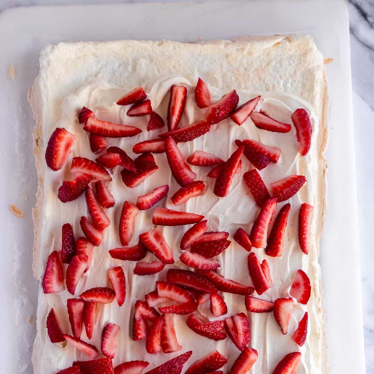 Spreading chantilly cream onto the pavlova, then topping with strawberries before rolling the meringue.