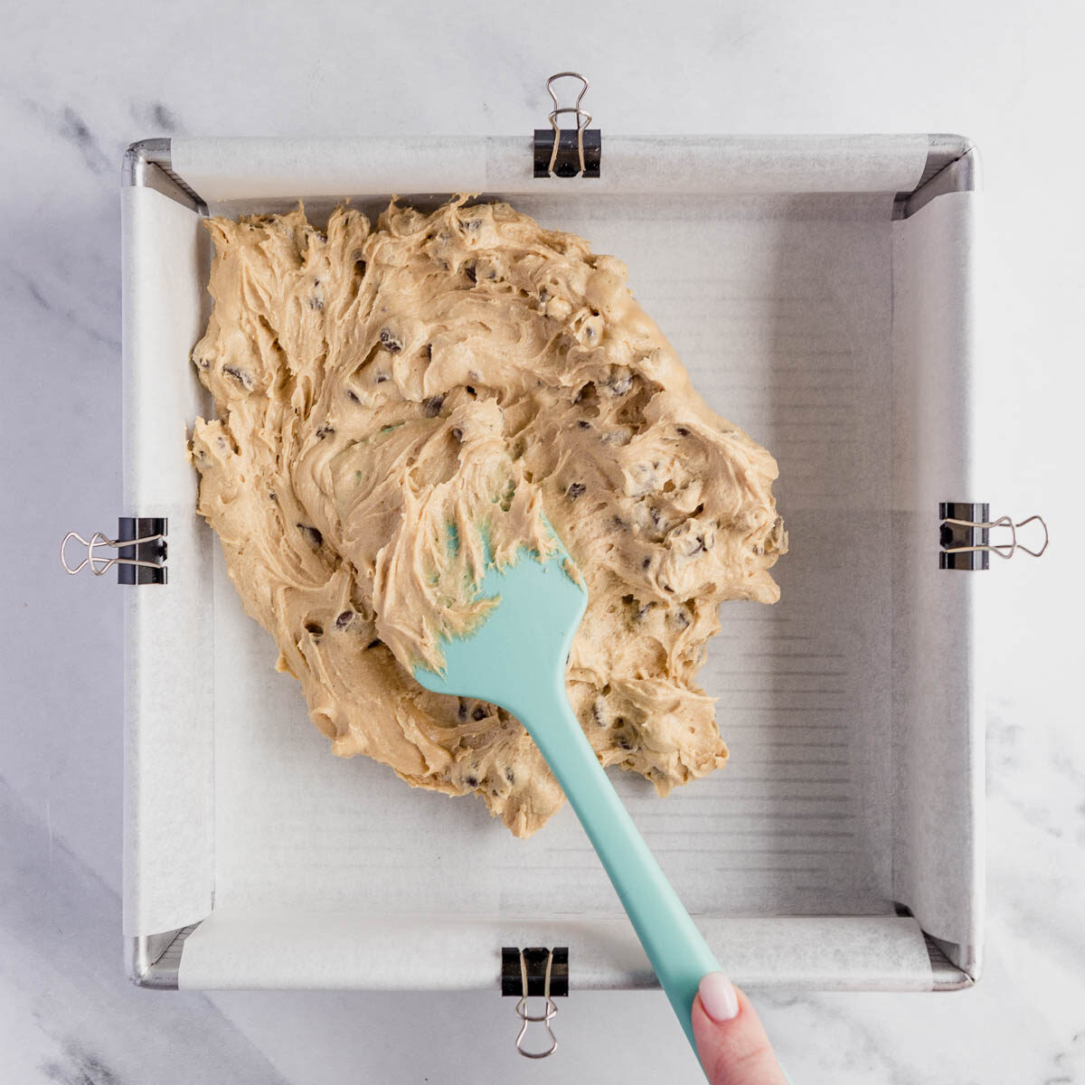 Spreading cookie dough into a lined pan, to make triple layer brownies.