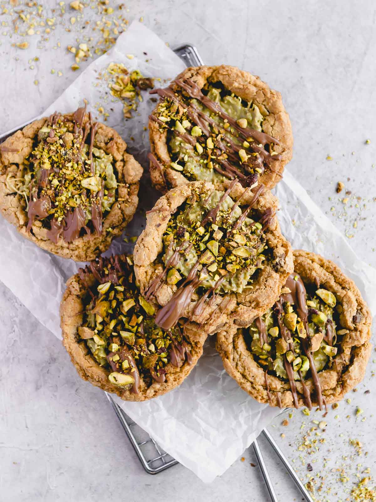 Five Dubai chocolate chip cookies on a tray, drizzled with chocolate and sprinkled with pistachios.