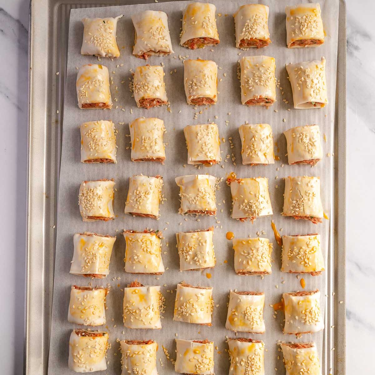 Brush the sausage rolls with egg wash and sprinkle with sesame seeds before baking.