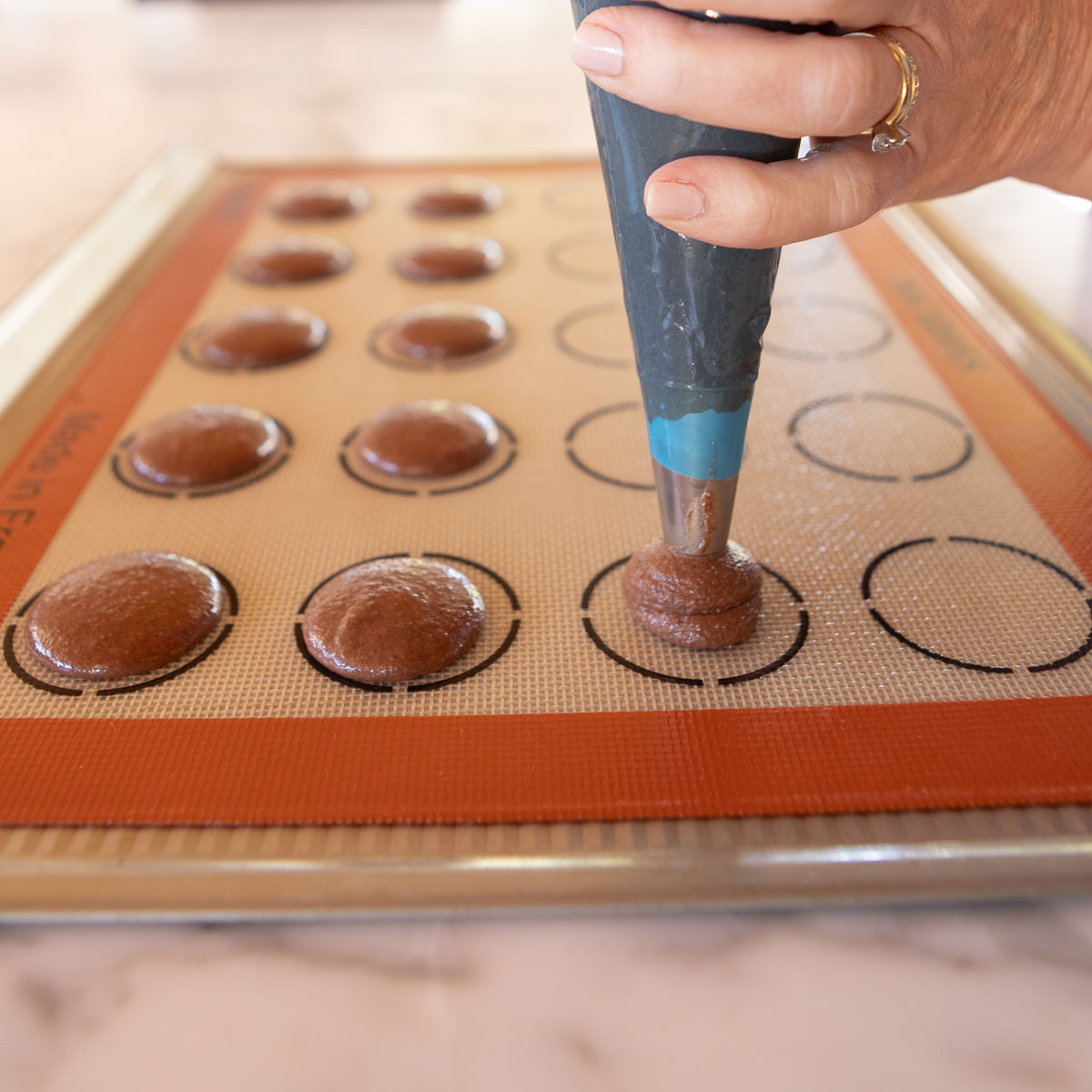 Piping macaron batter onto a silpat mat with circle guides.